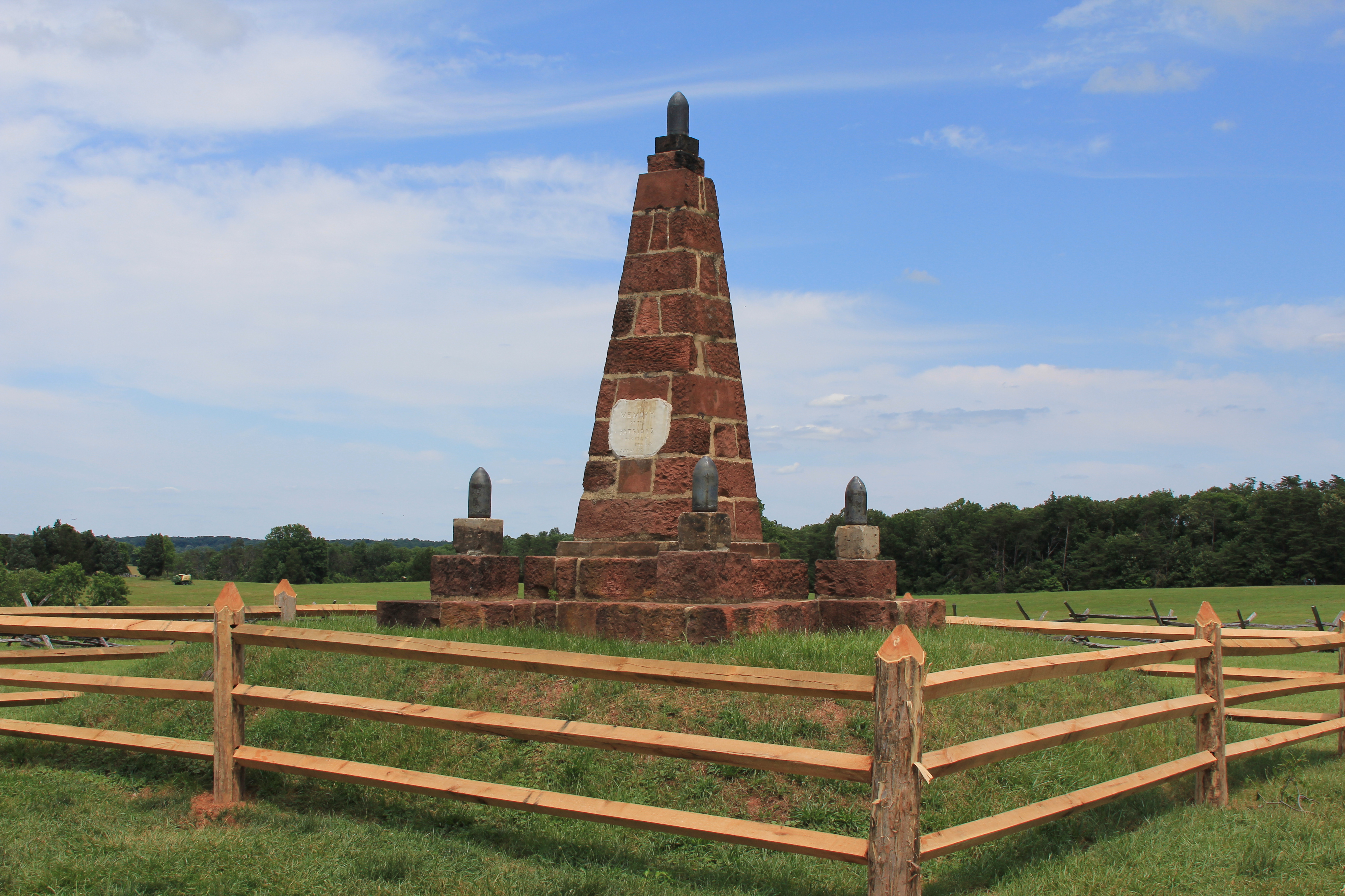 Red sandstone obelisk surrounded by post and rail fence.