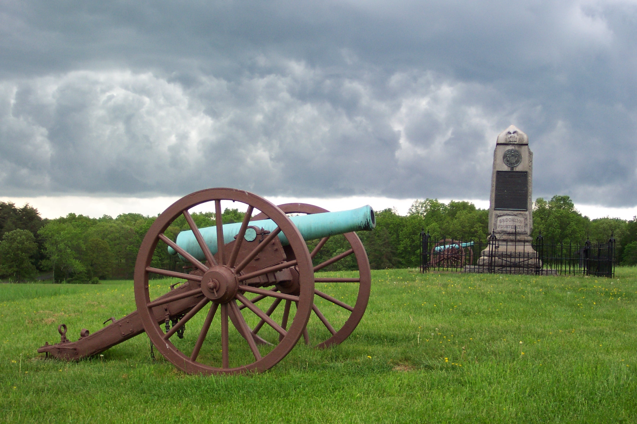 Civil War cannon and granite and bronze monument under a cloudy sky.