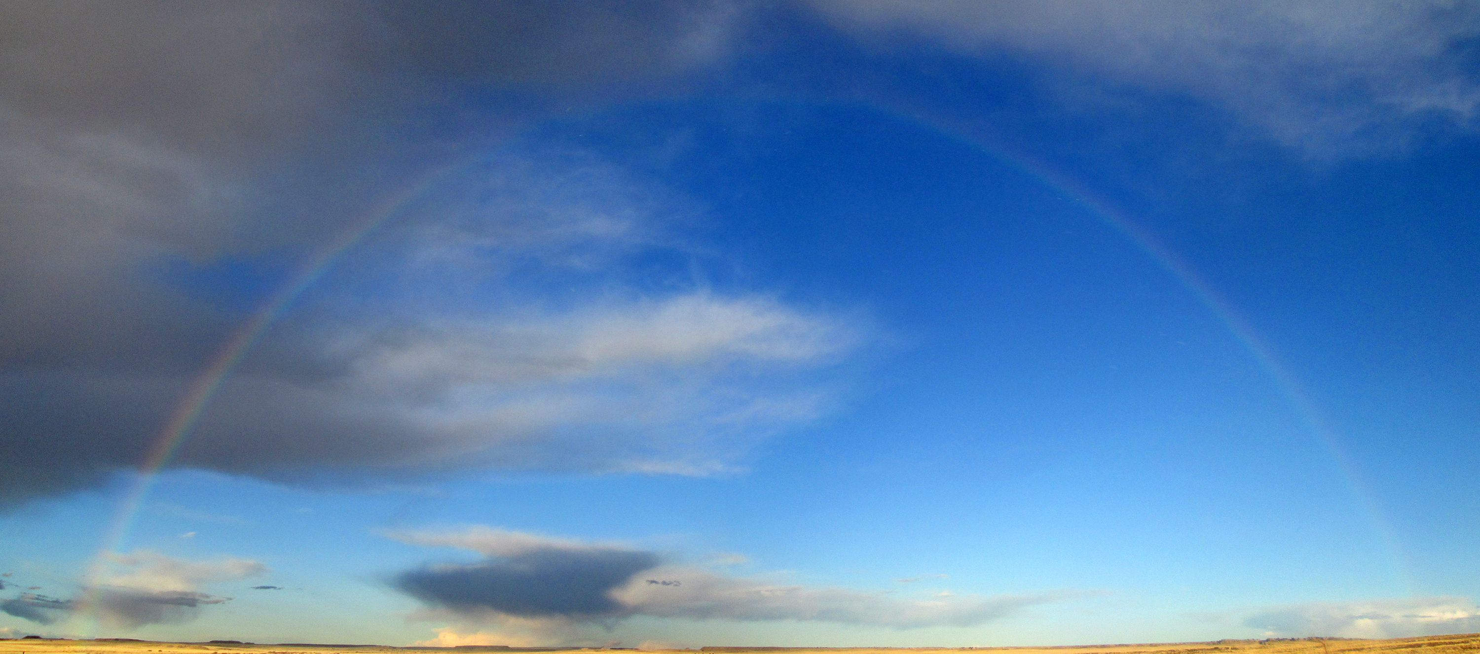 A full rainbow arches over the open grassland.