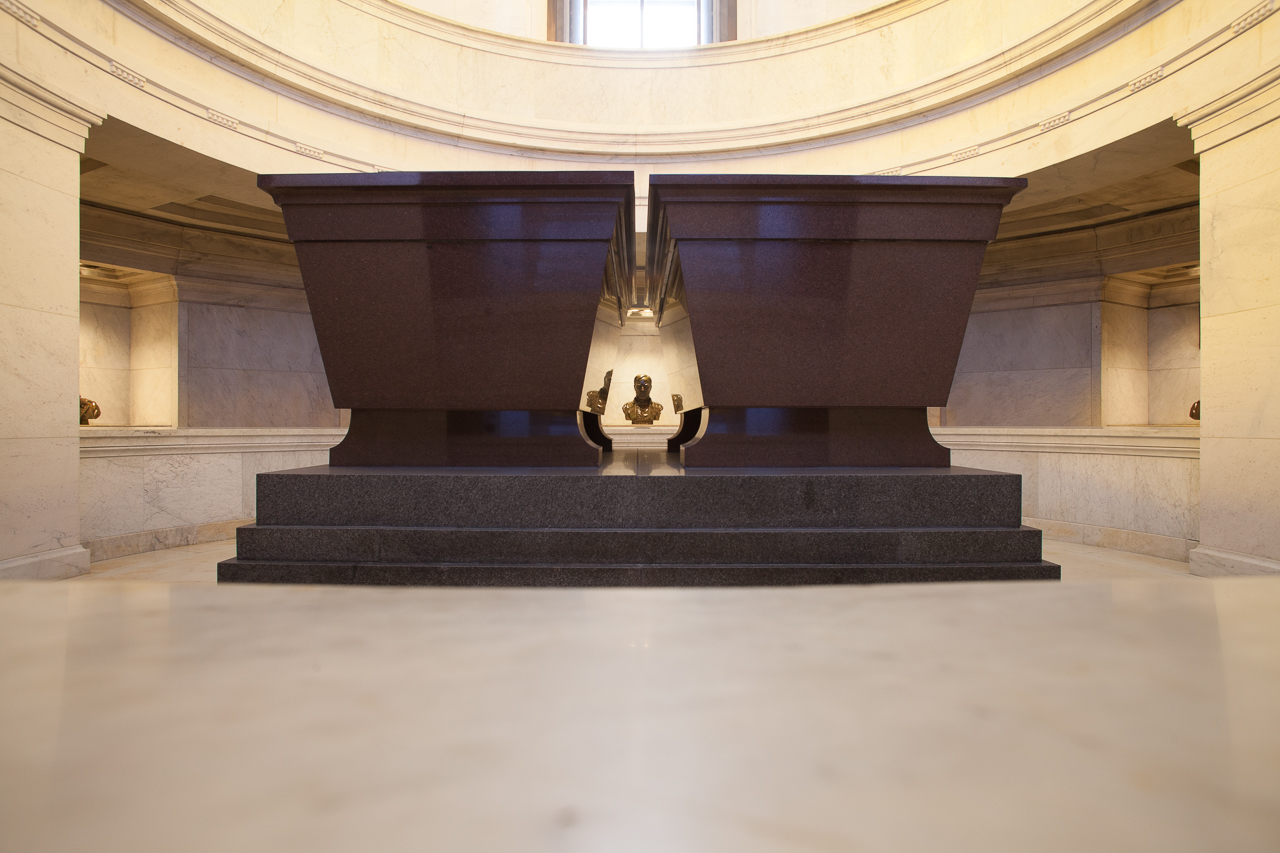 Two red stone sarcophagi are in a crypt. A bust of General Sherman can be seen in the distance.