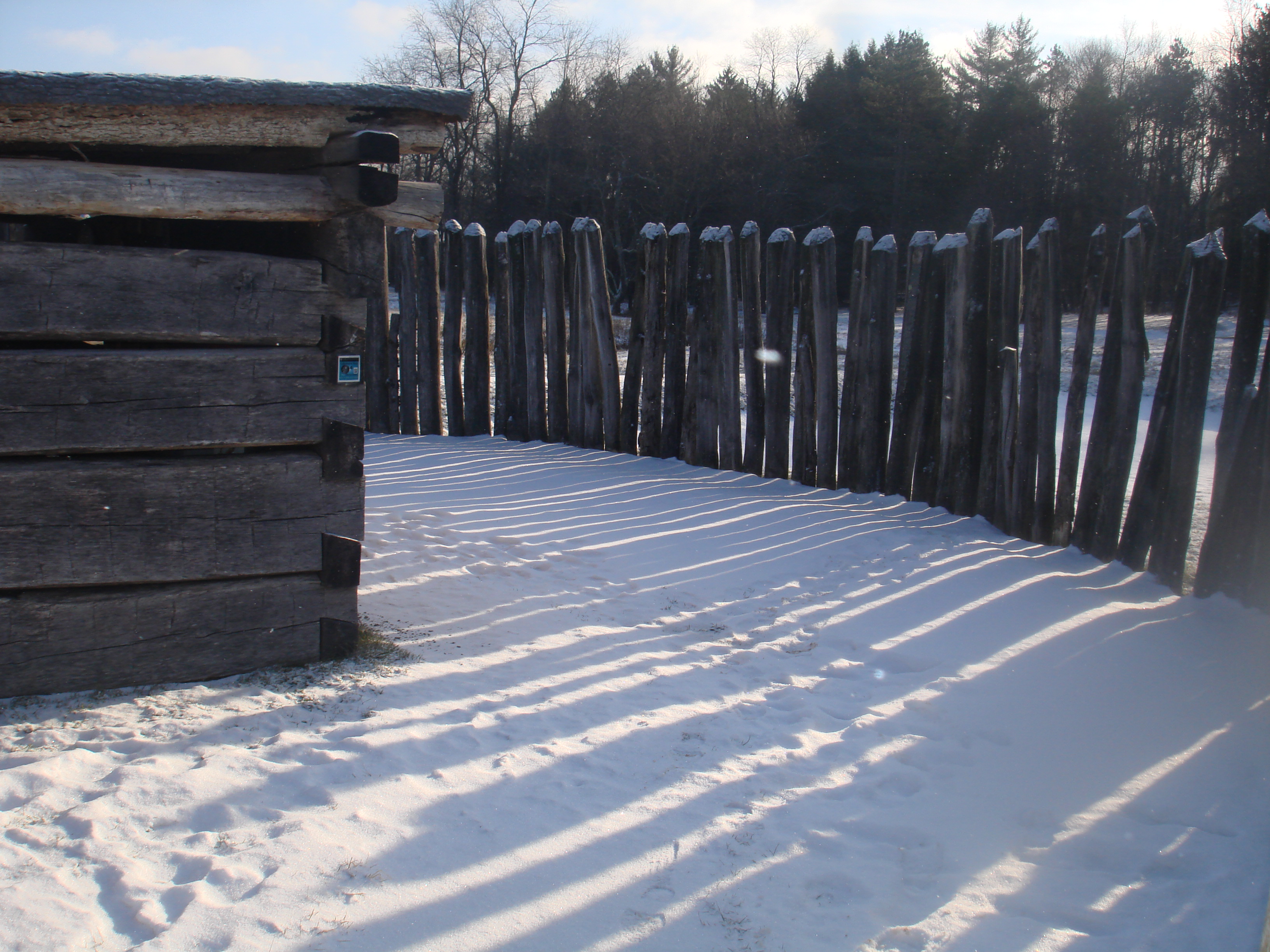 cabin and stockade casting shadows on the snow