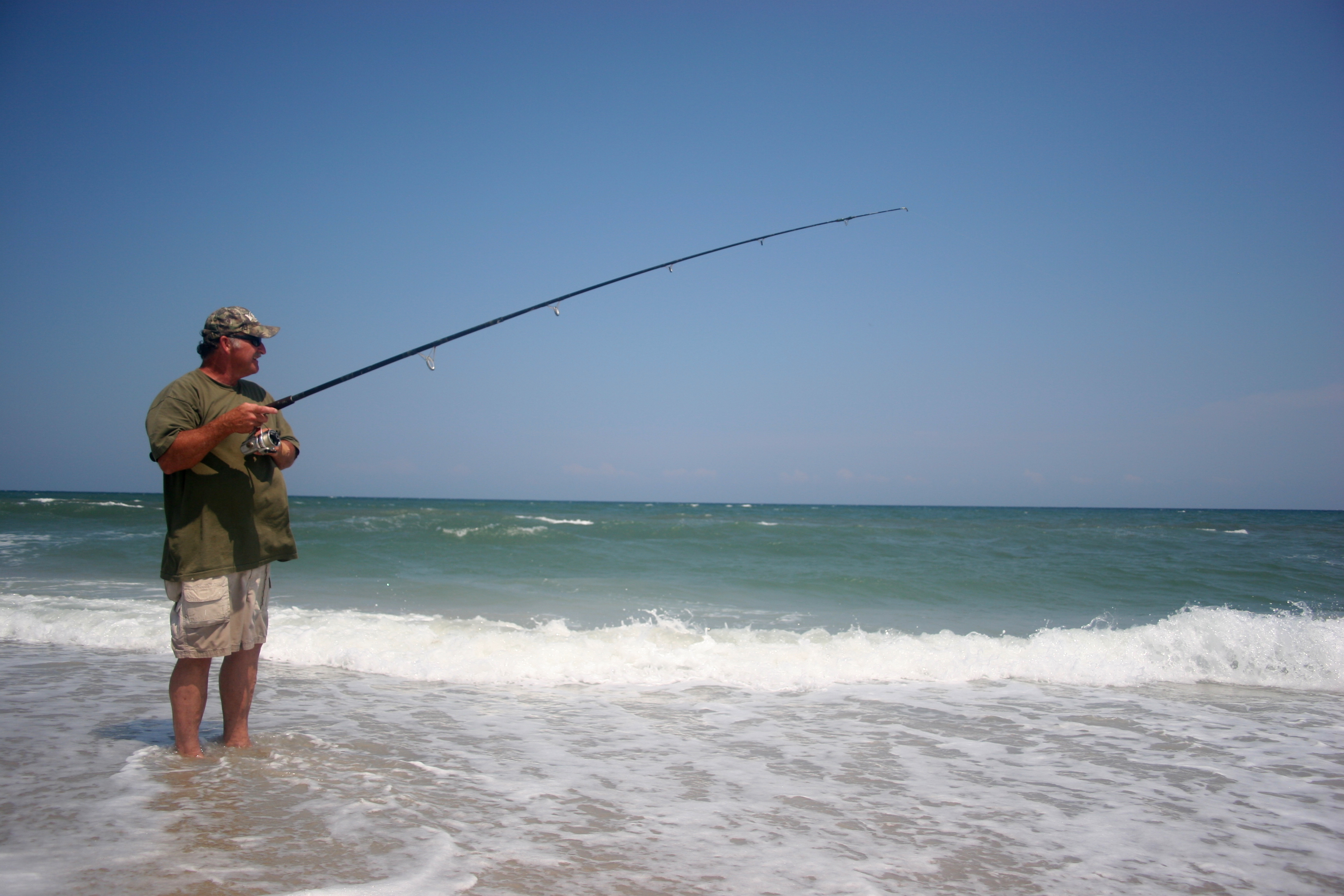 A surf fisherman stands in the water holding his surf rod and watching the waves