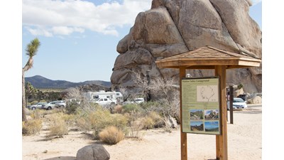 A Campground Board in the foreground with a parking lot in the background.