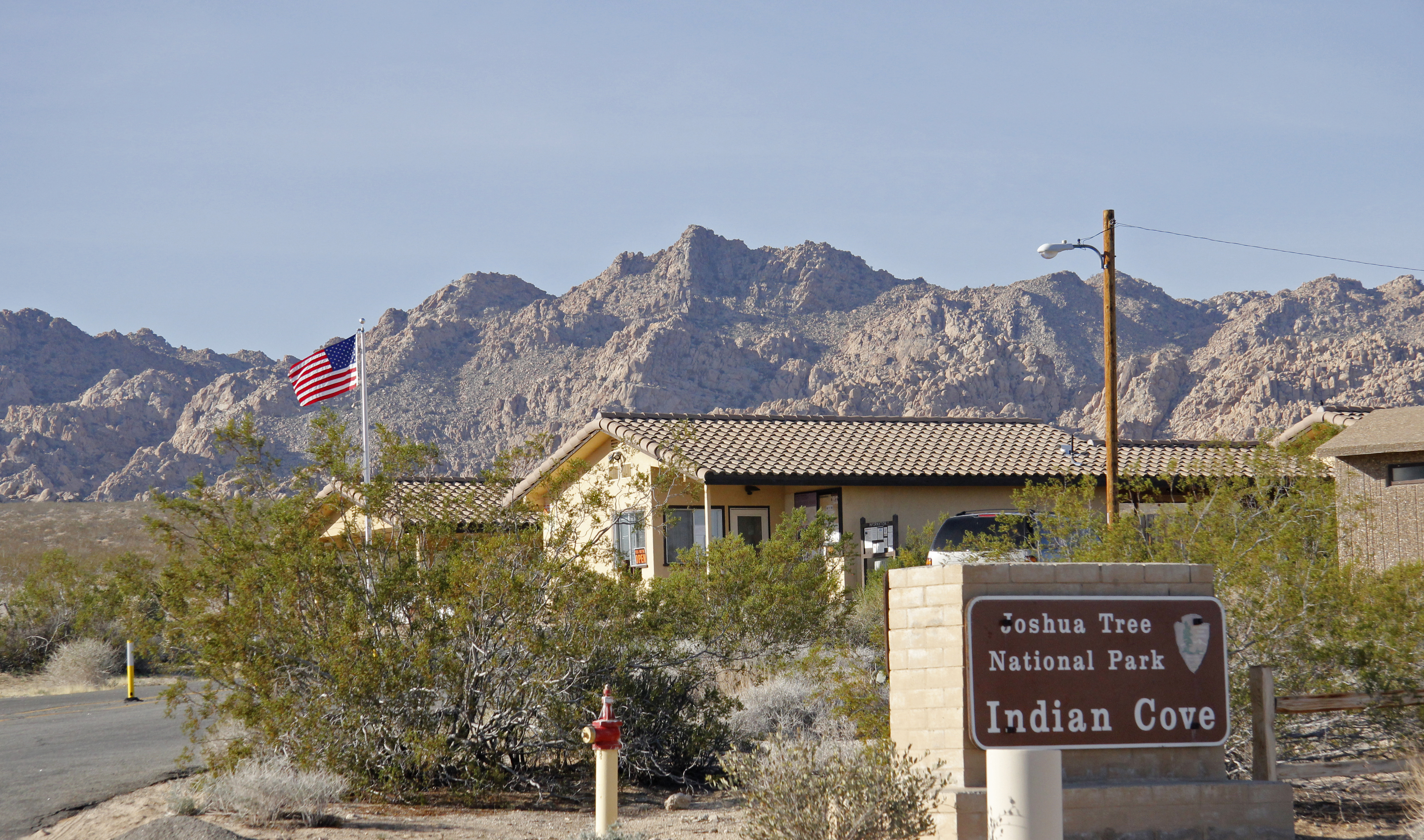 A sign that reads 'Joshua Tree National Park... Indian Cove'. Behind it is a building.