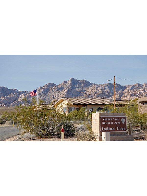 A sign that reads 'Joshua Tree National Park... Indian Cove'. Behind it is a building.