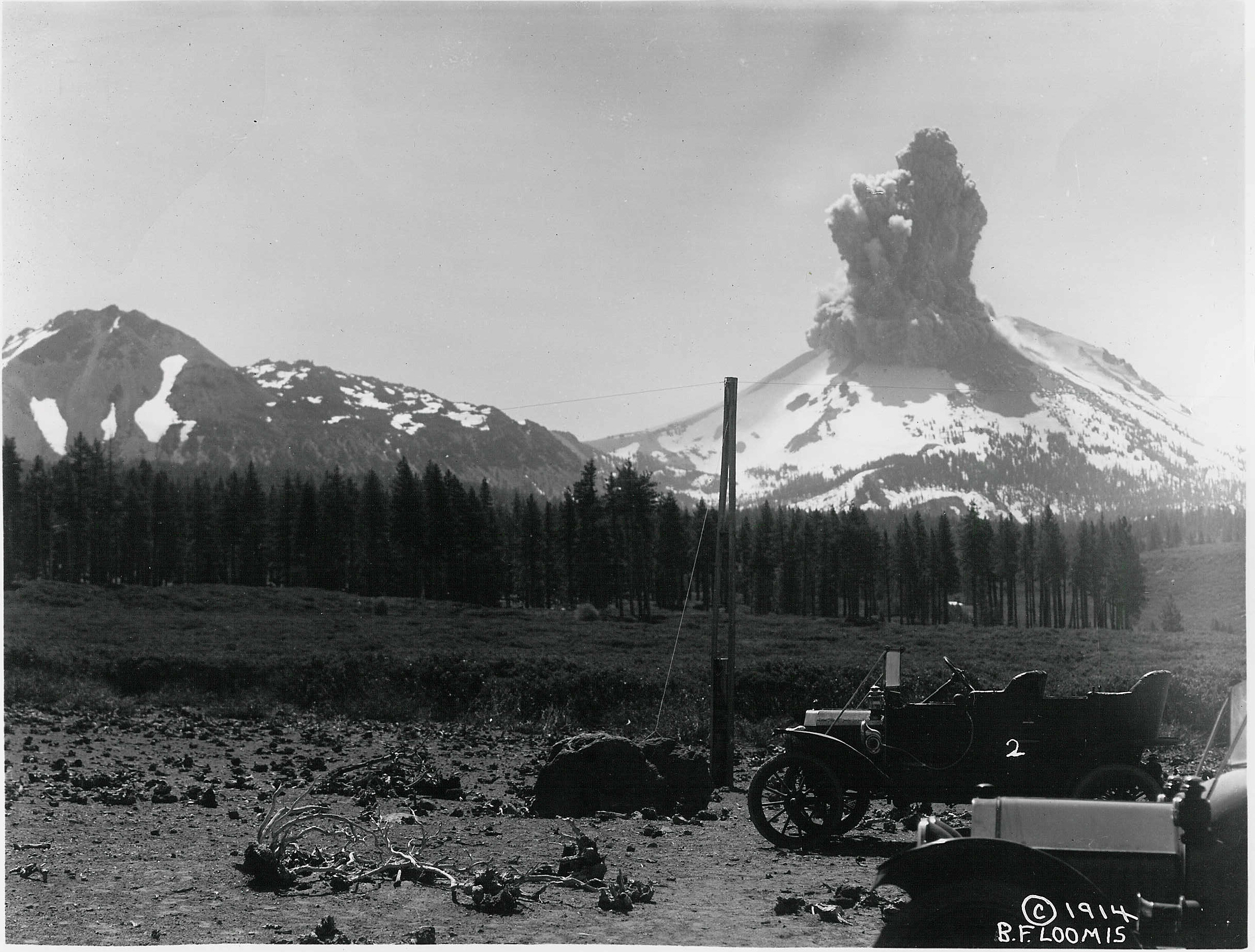 An ash cloud rises above a volcano with an early 19th century vehicle at the forefront.