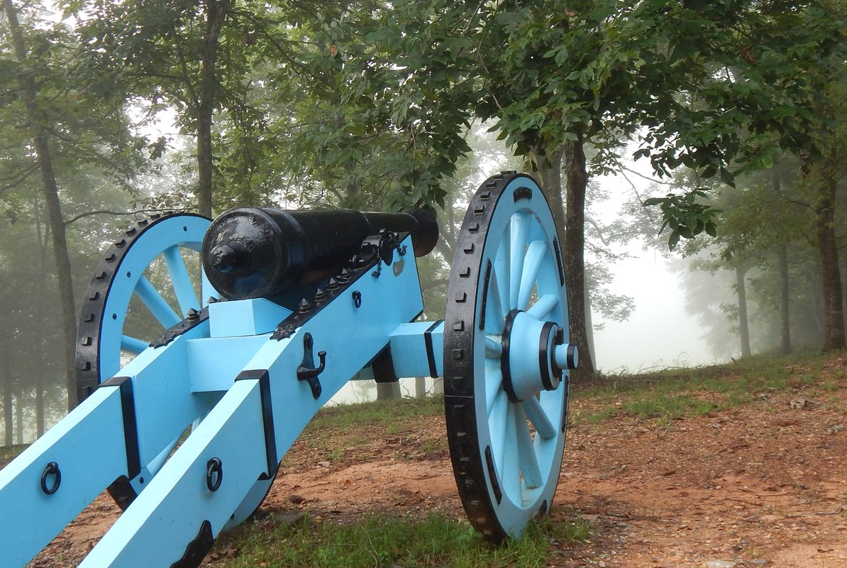 A blue painted 6-pounder cannon sits on hill facing the battlefield 