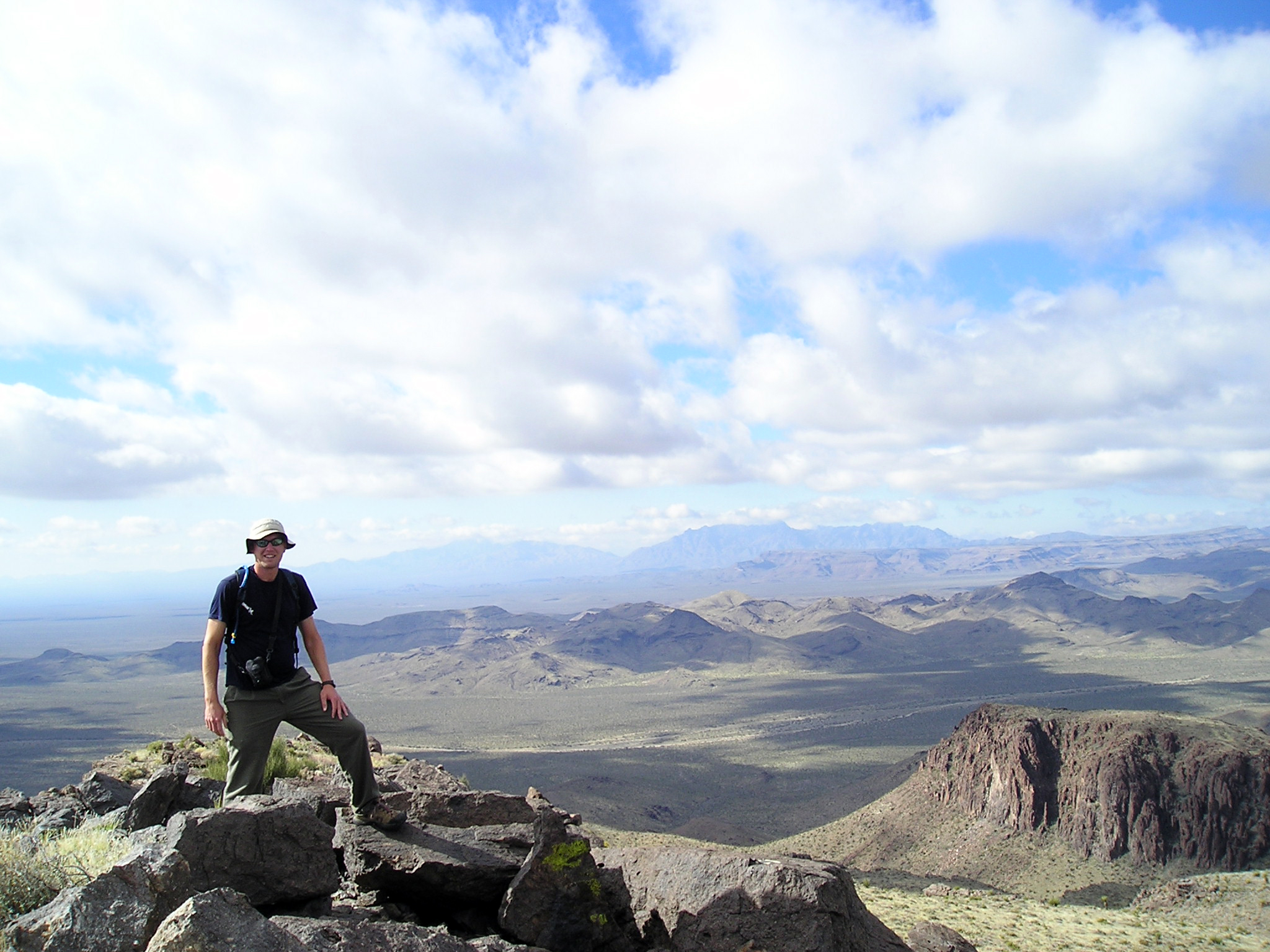A man standing on a mountain peak in front of a wide desert landscape
