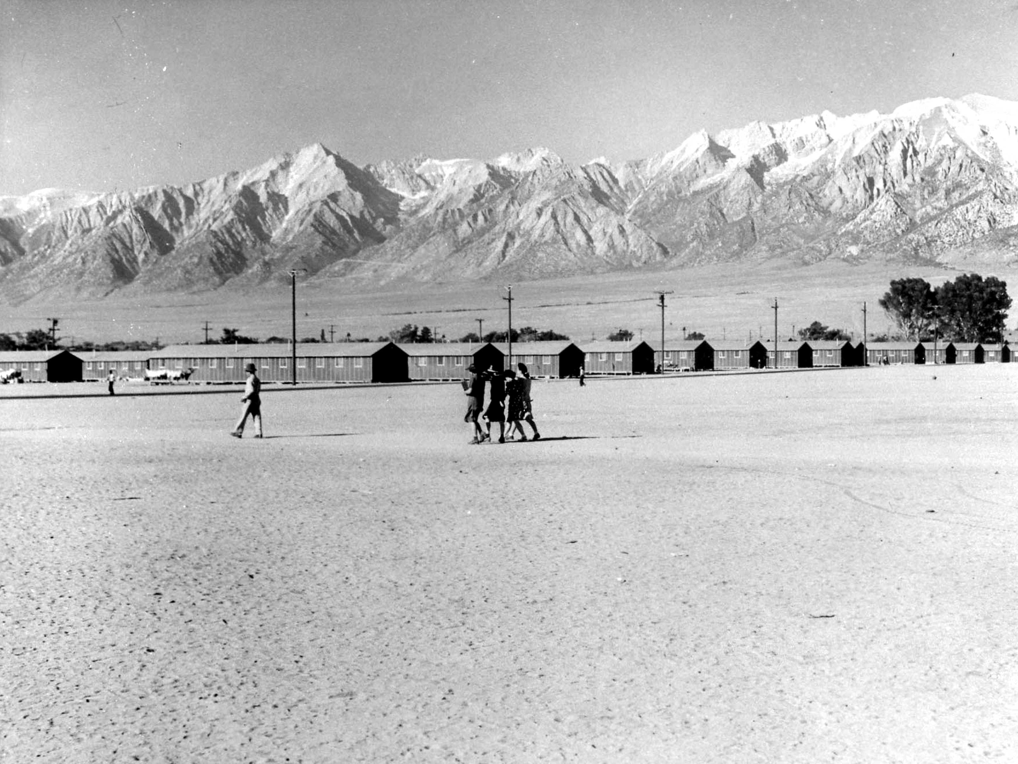 People walk to barracks framed by mountain peaks.