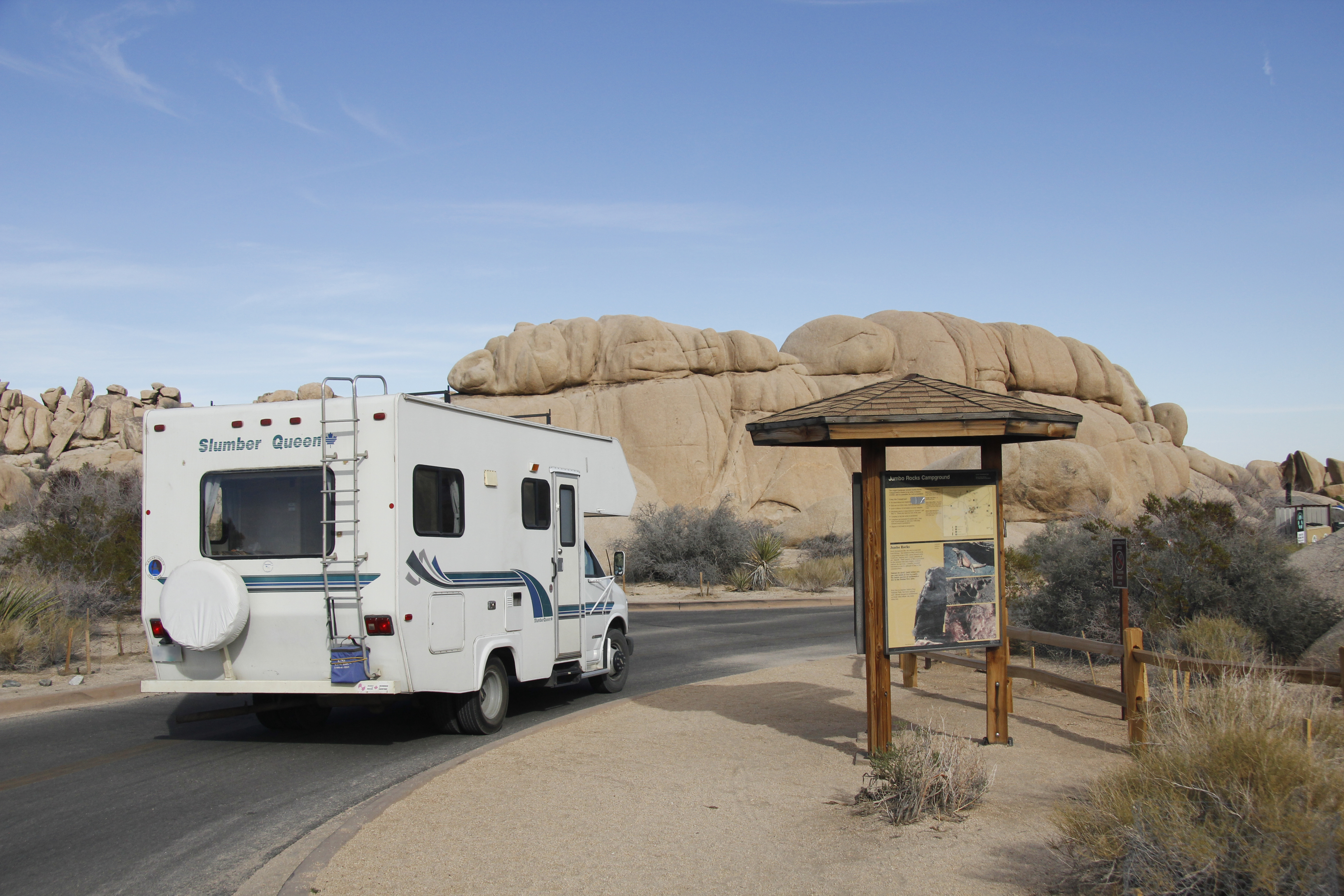An RV drives past an campground information board.
