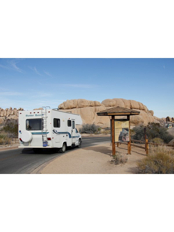 An RV drives past an campground information board.