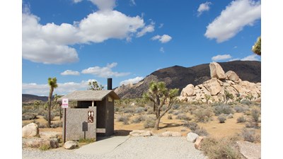 A small wheel chair accessible vault toilet and parking space.