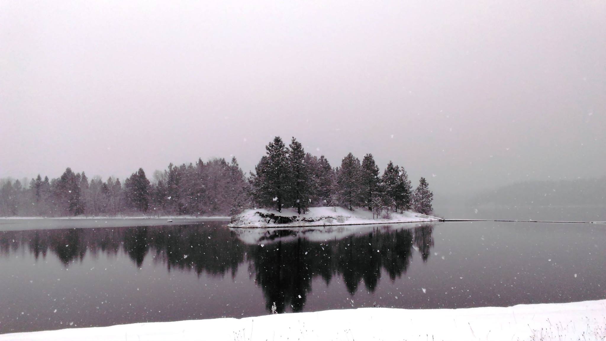 Snow falls over a small peninsula with its clear reflection over the waters.