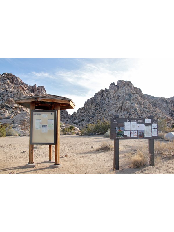 Two informational boards at the sheep pass group campground with large rocky outcrops behind them.