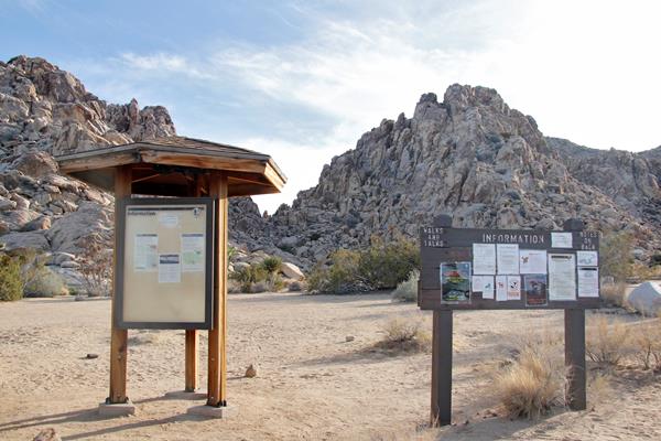 Two informational boards at the sheep pass group campground with large rocky outcrops behind them.