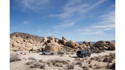 Two cars are in a small, unpaved parking lot.