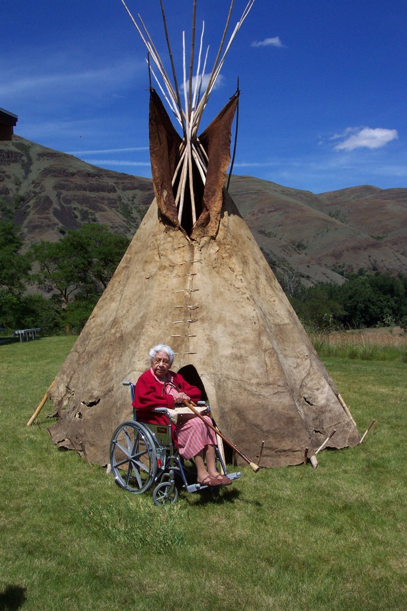 Buffalo Hide Tipi Elder (Mylie Lawyer) sitting in front of Old Buffalo hide tipi.