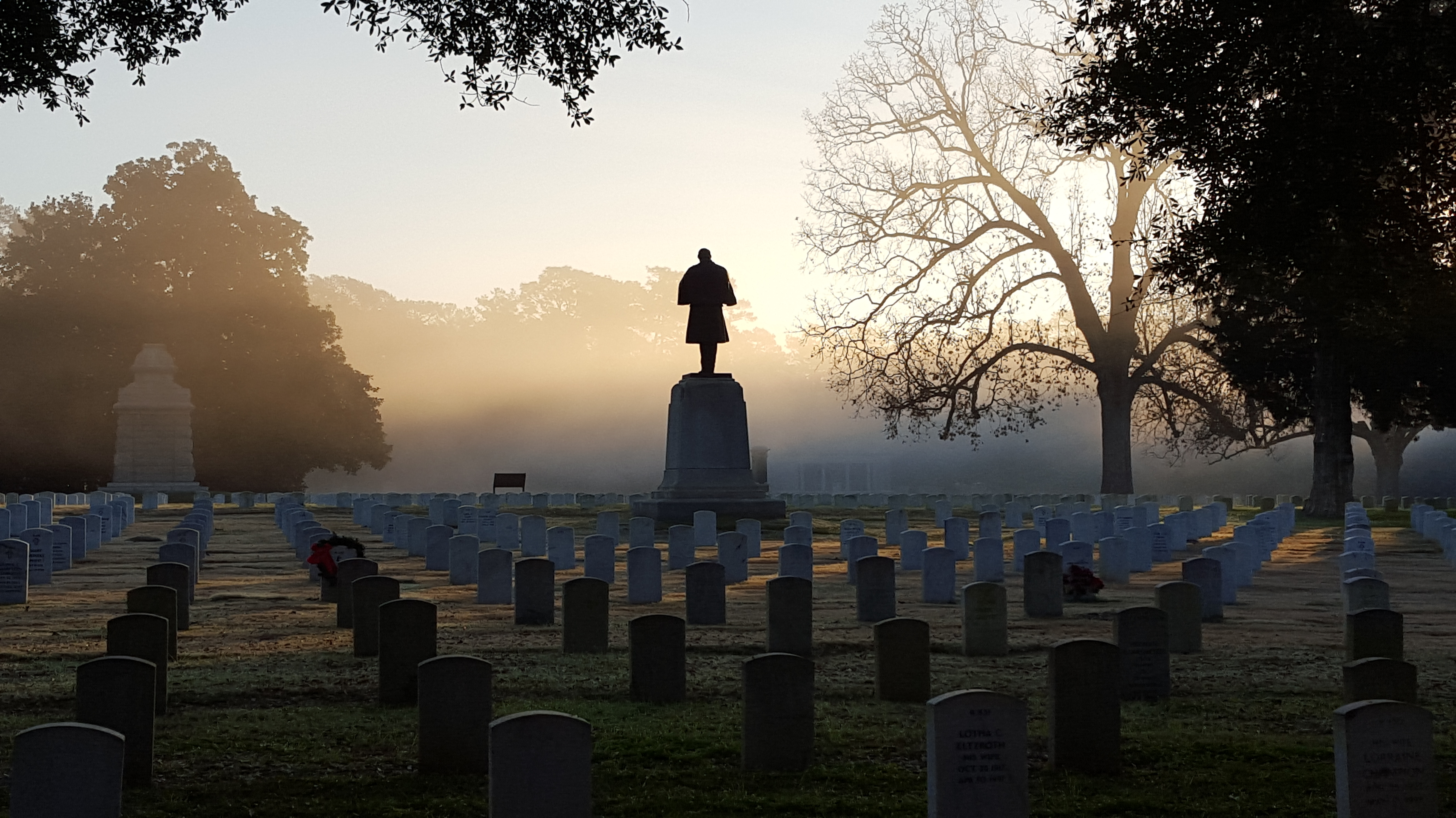 Fog rests on a stone monument of a Civil War soldier standing among hundreds of graves.