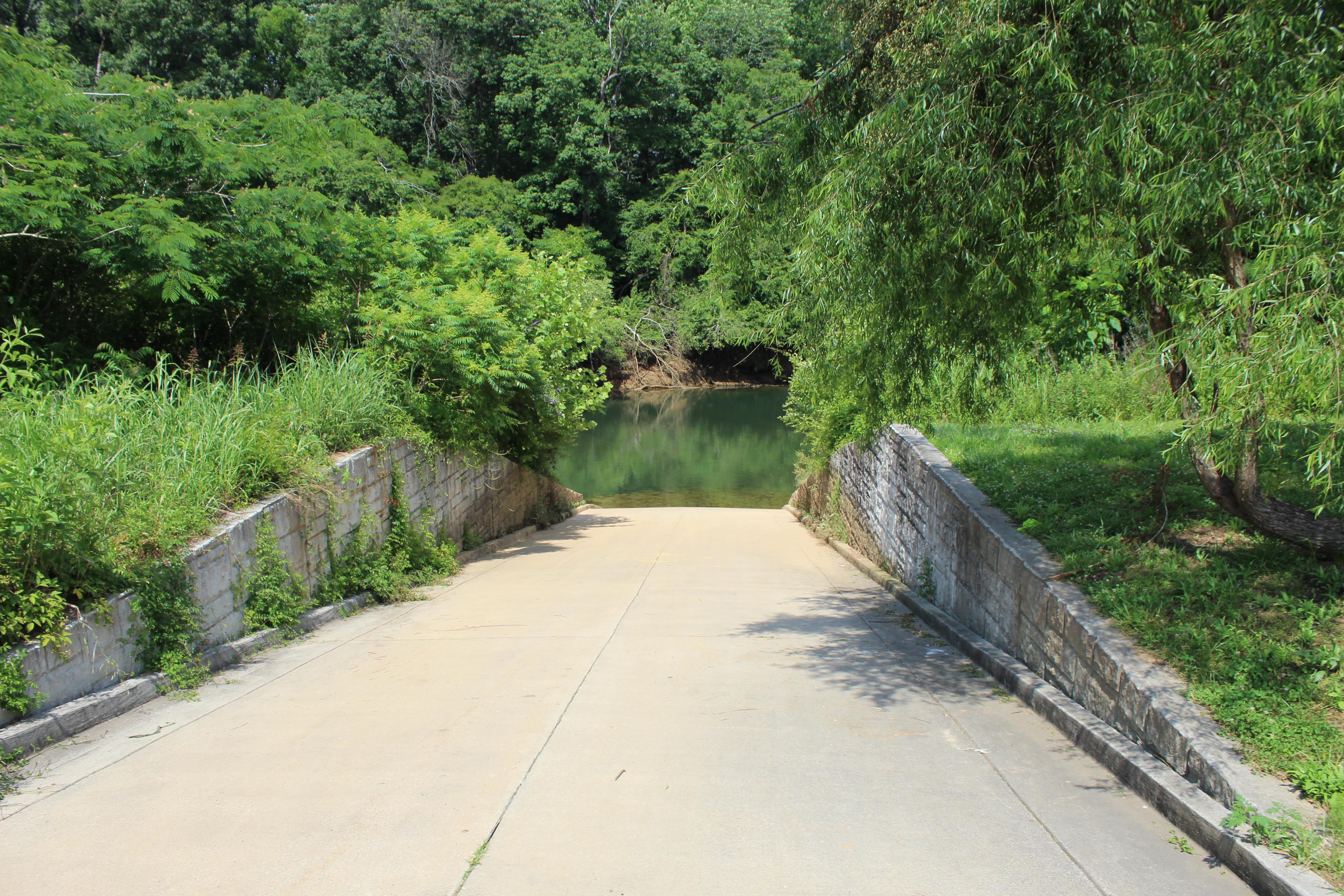 Looking down boat ramp with retaining walls on both sides and trees on the other side of the river.