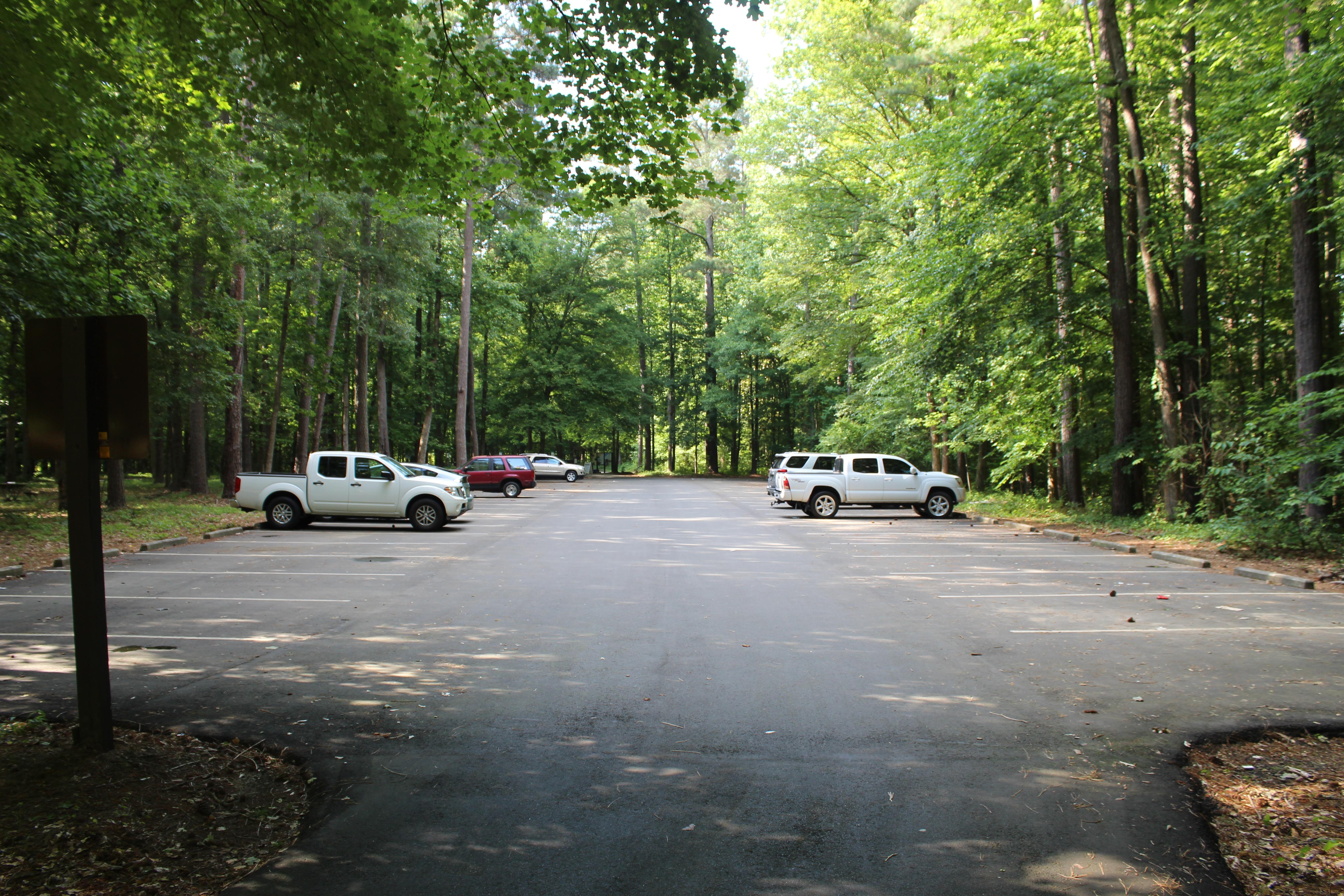 Paved parking lot with cars and trucks on either side in a grove of trees.