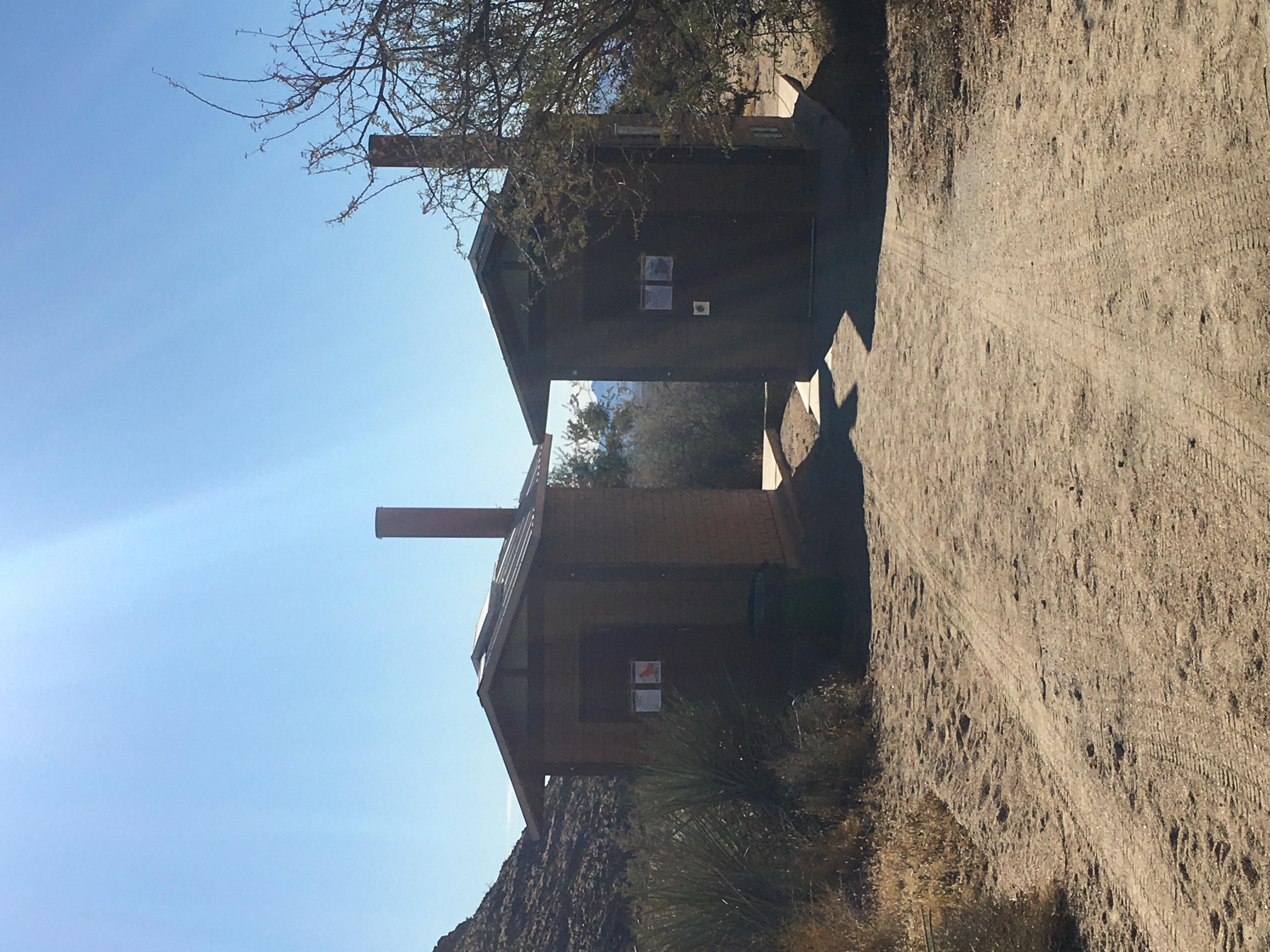 Two pit toilets stand between desert shrubbery at the group campsite.