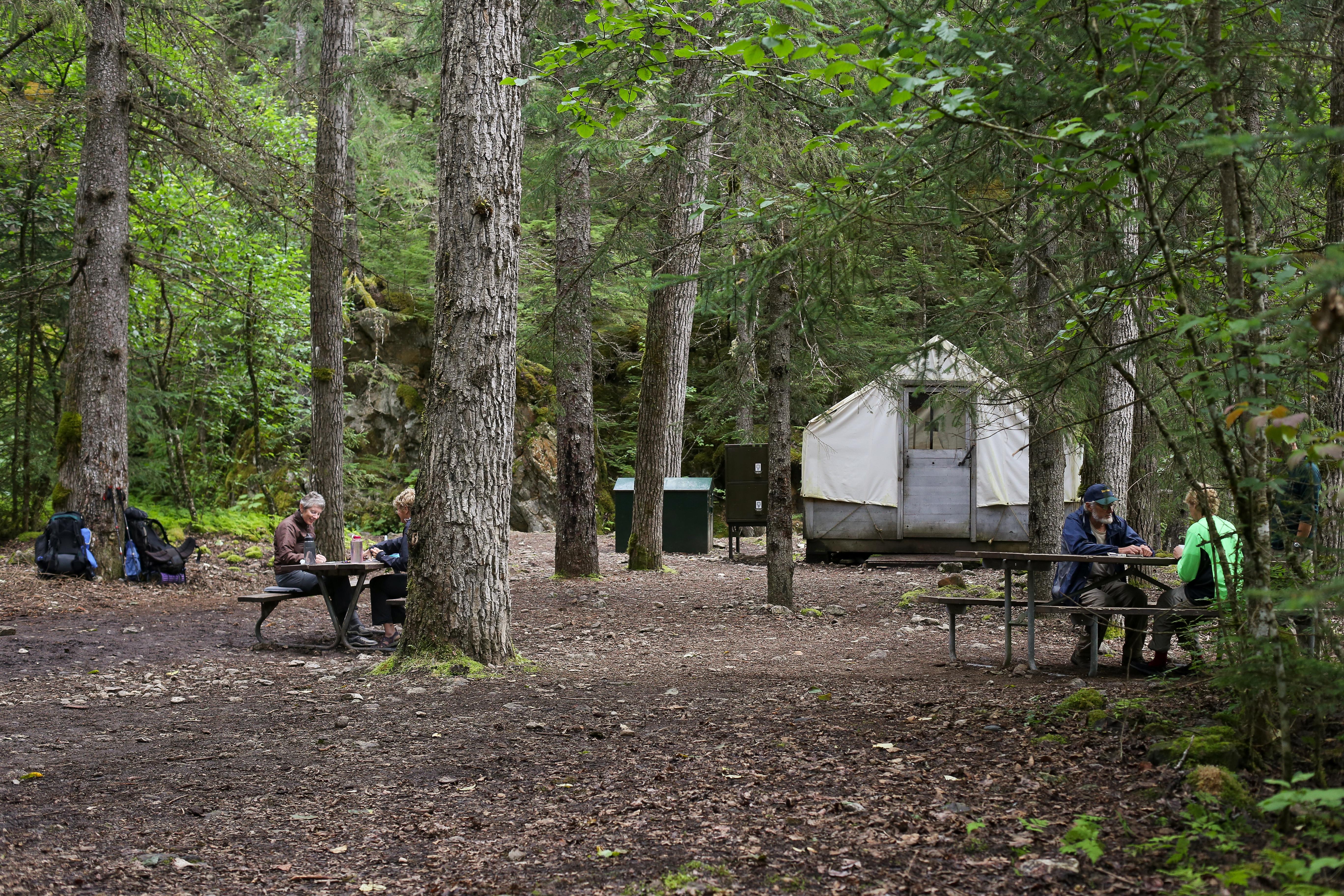 People sit at picnic tables in front of a white wall tent