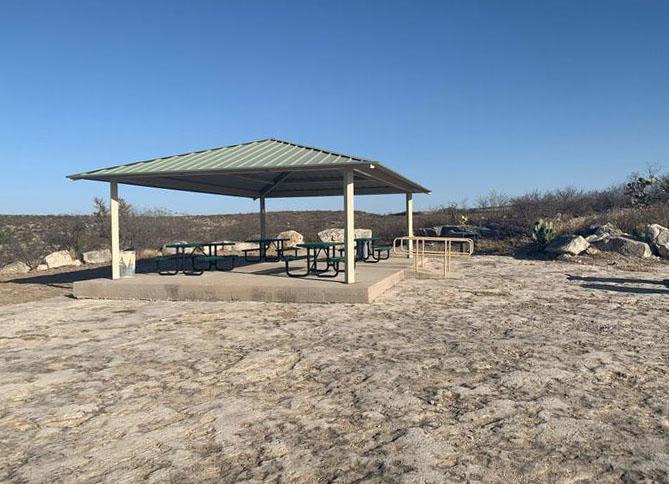 Tin-roofed pavilion with cement floor and accessibility ramp surrounded by flat ground.