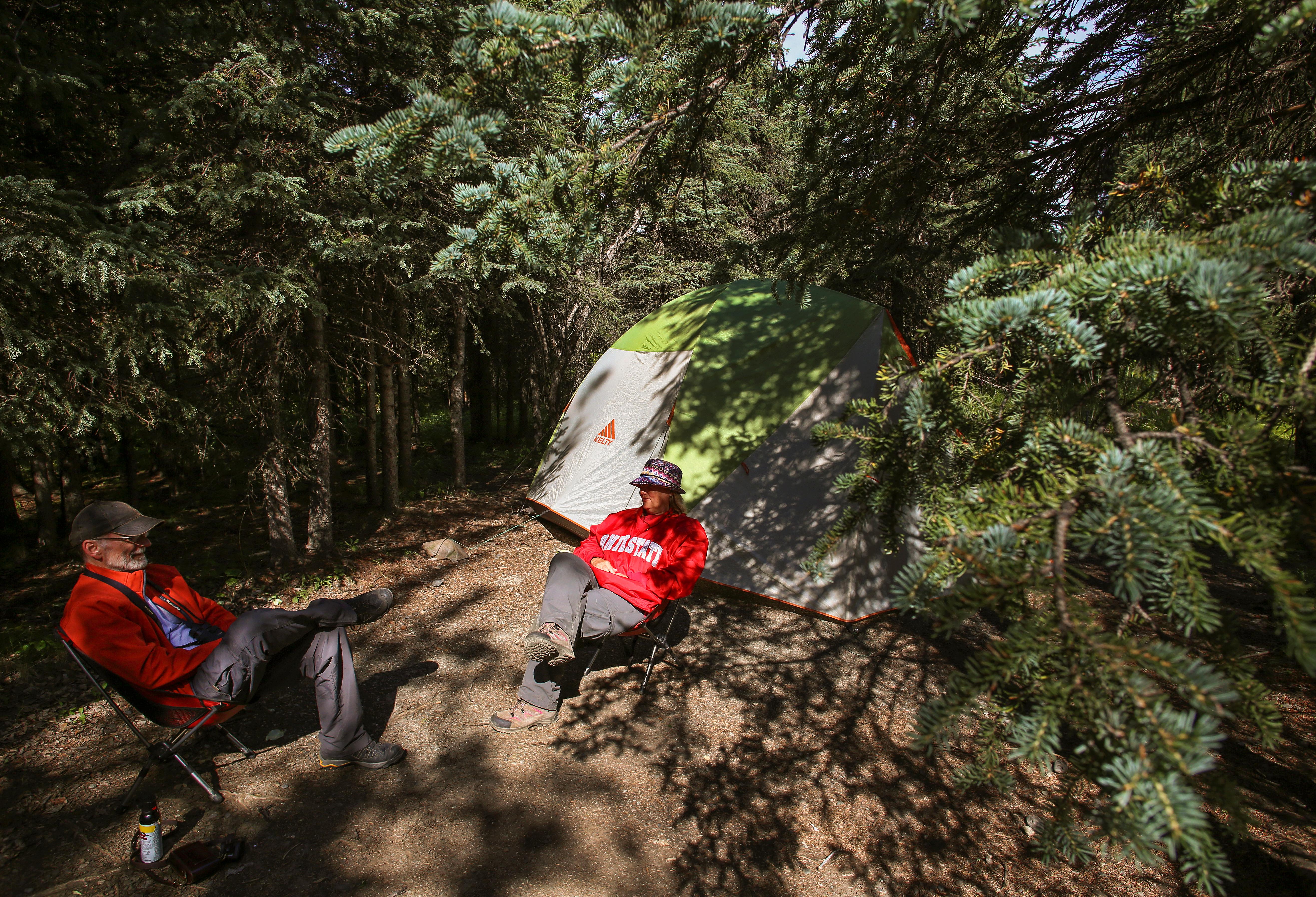 two people sitting in chairs outside of their tent in a forest