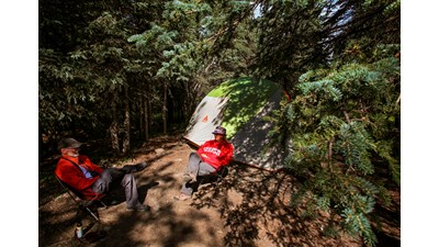 two people sitting in chairs outside of their tent in a forest