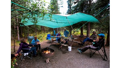 several people in camp chairs around a fire, under a tarp hung from trees