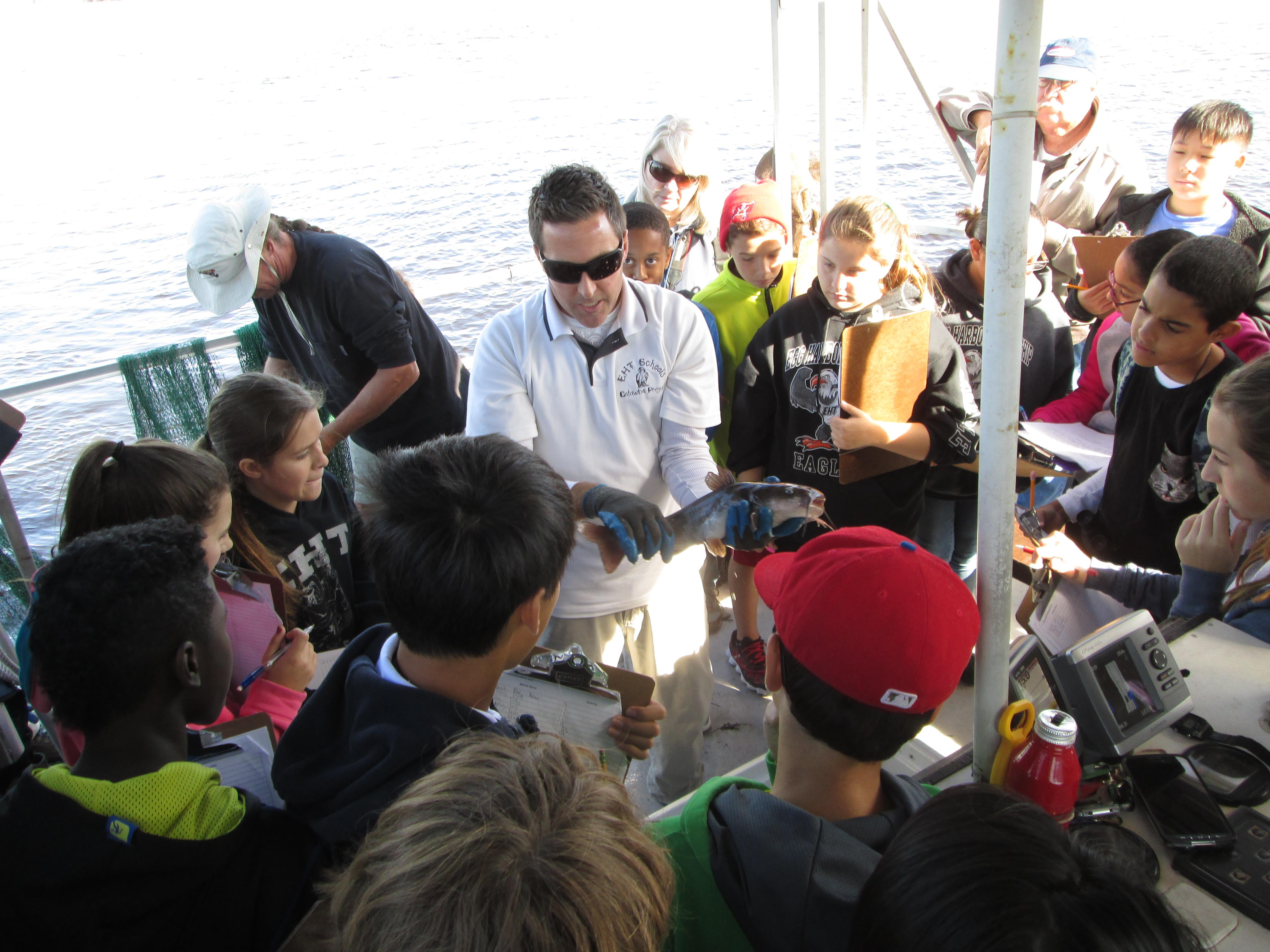 School group examines a fish held by the instructor.
