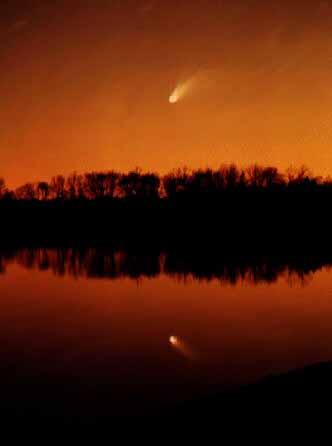 Bright white comet in the early night sky reflects over the river.