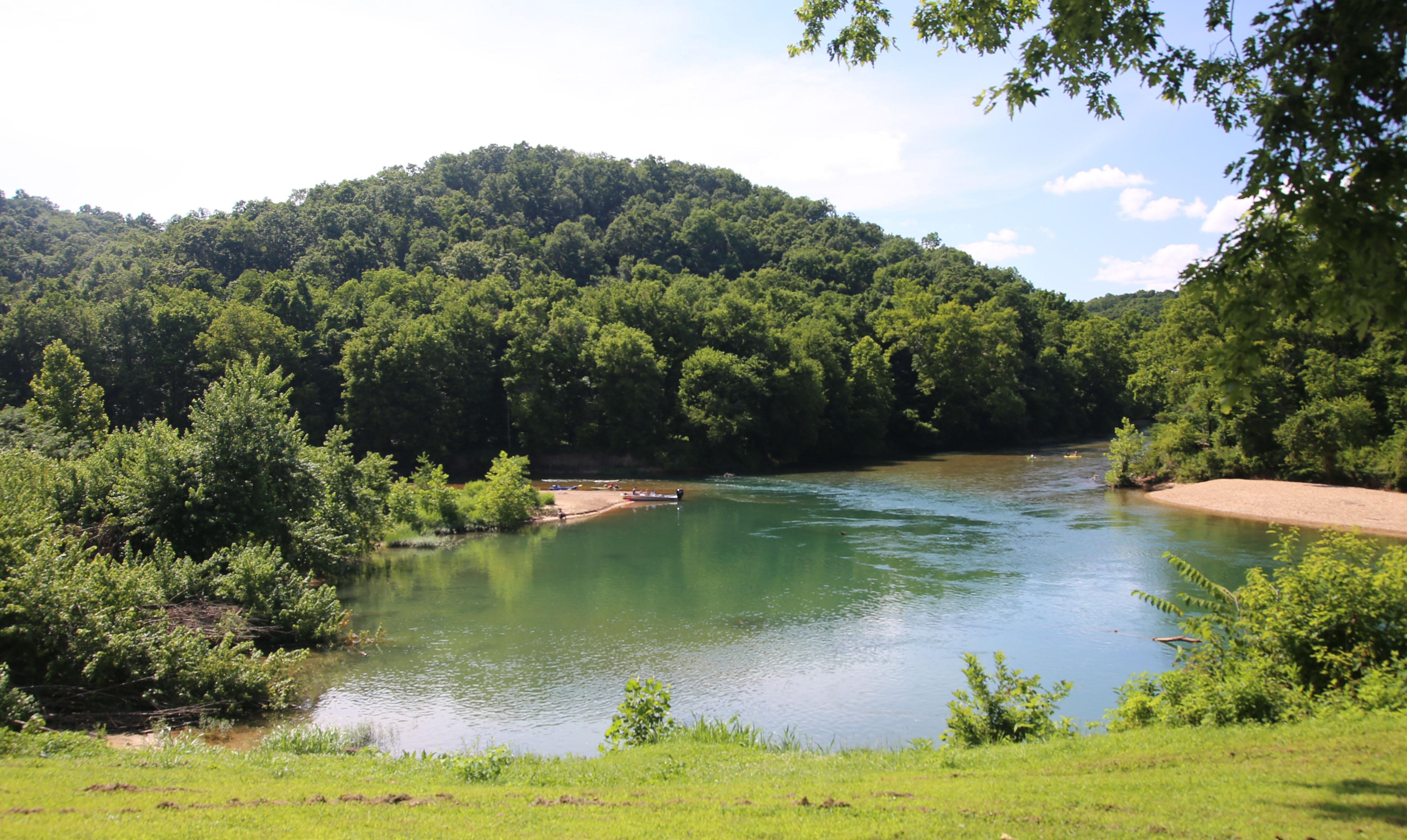 two clear stream join with blue pool in middle of picture, hillsides with green trees, gravel bar