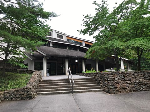Entrance of the Folk Art Center: a concrete stairway between stone walls leading to a two-story building among trees
