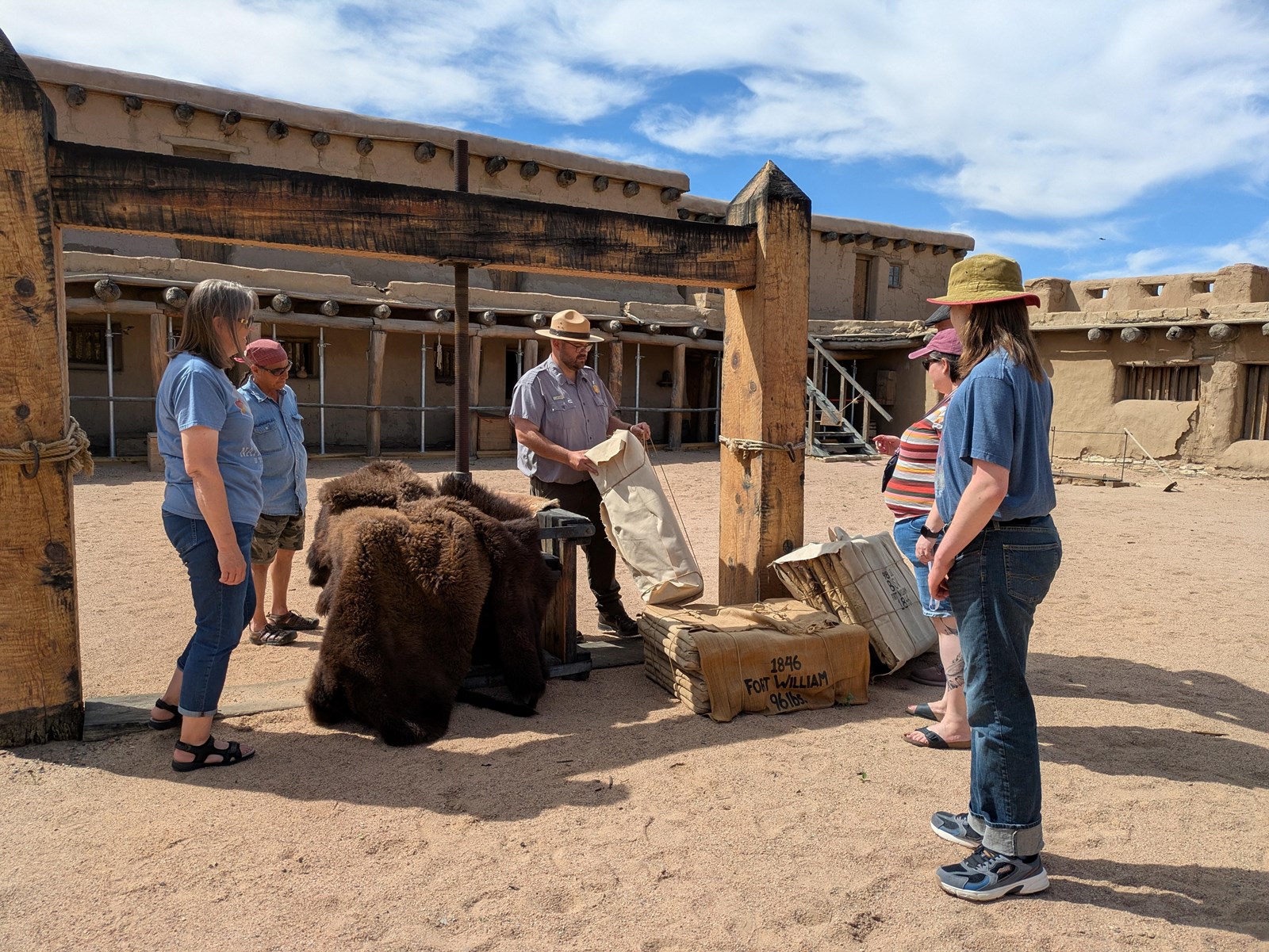 A group of visitors stand around a large wooden apparatus in a plaza courtyard.