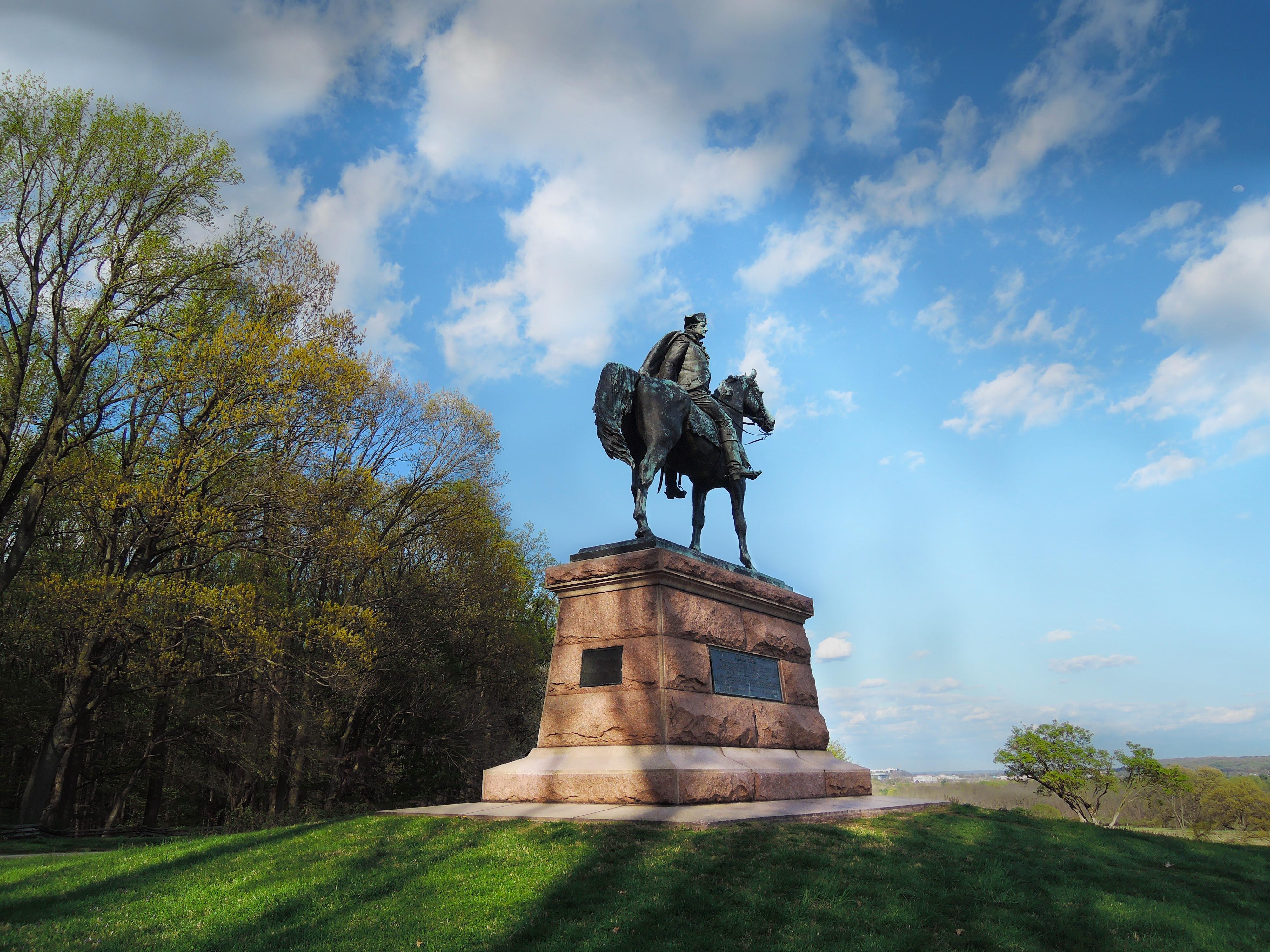 outdoors, monument, statue, man on horse, grass, trees, clouds.