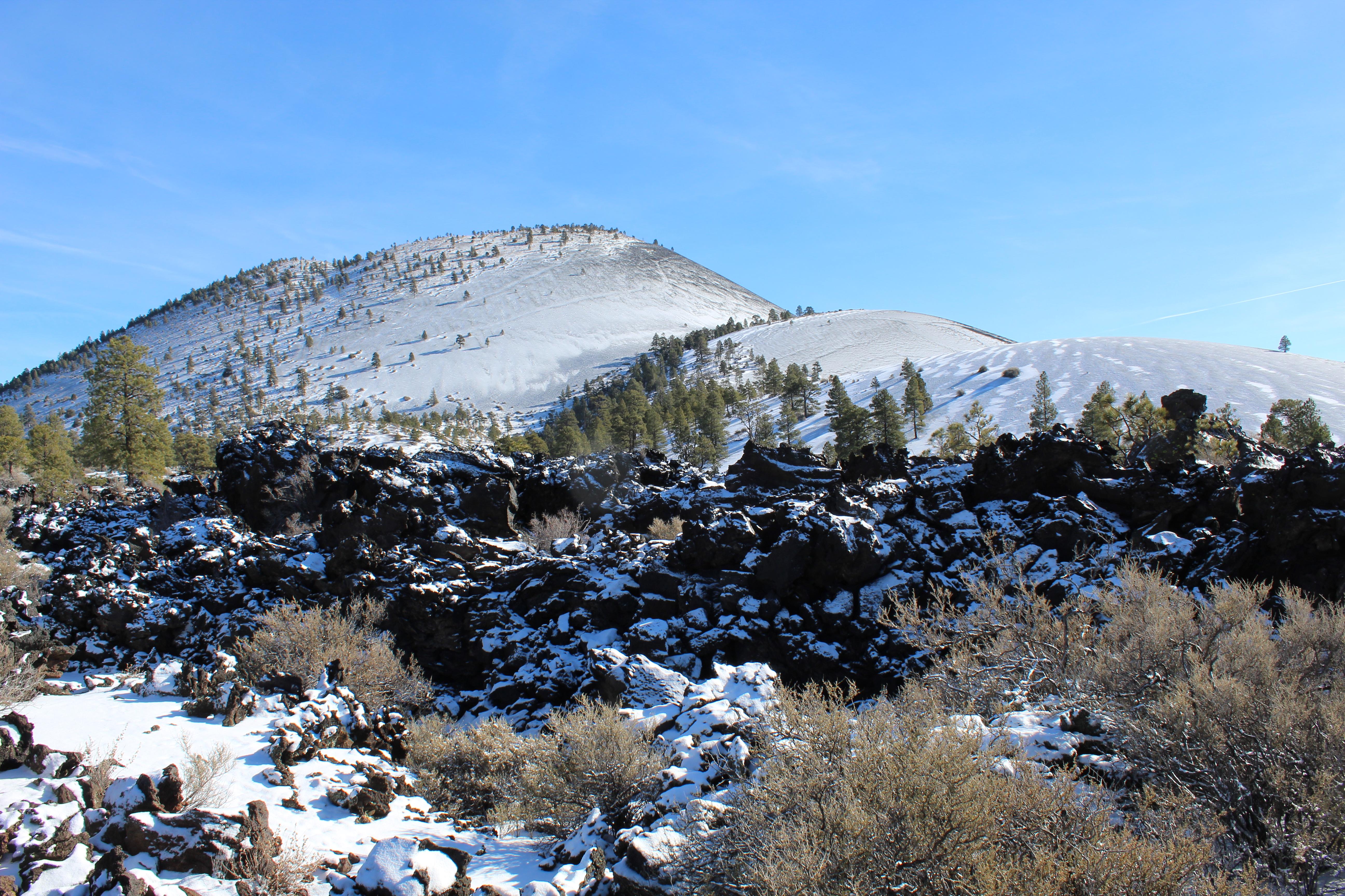 A snow-covered cinder cone and lava flow under a clear blue sky