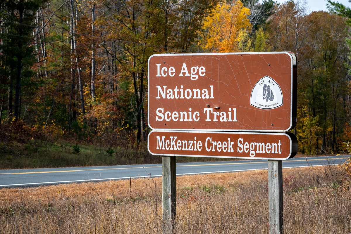Photograph of “Ice Age Trail” sign surrounded by a forest with autumn foliage.