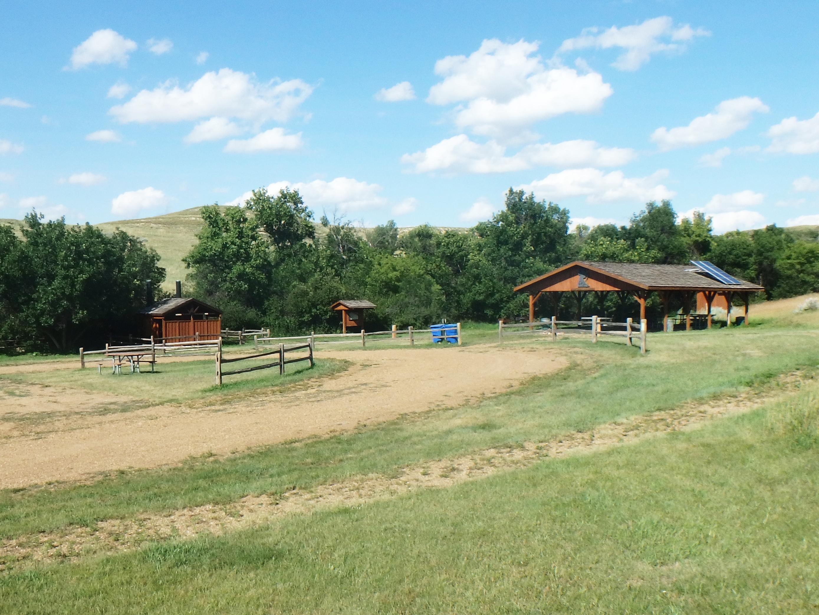 A wood pavilion and restroom at the edge of a curved gravel drive with green grass