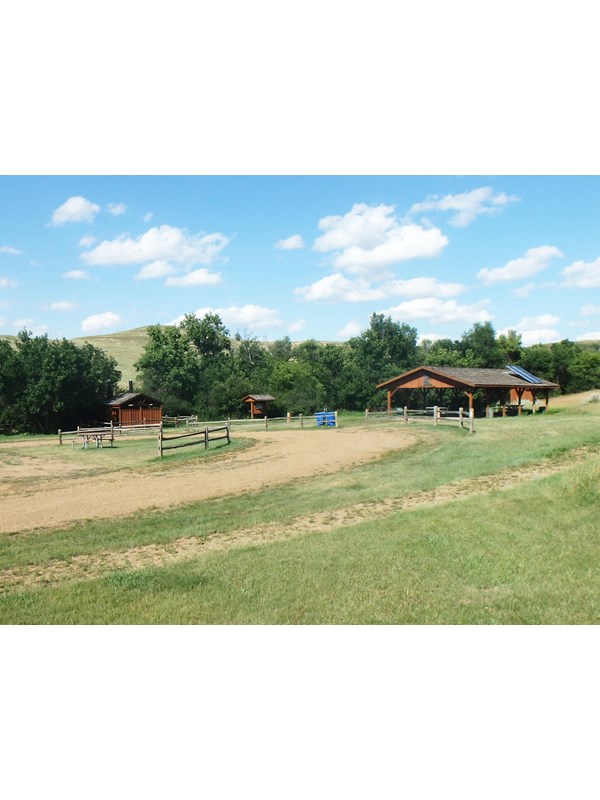 A wood pavilion and restroom at the edge of a curved gravel drive with green grass
