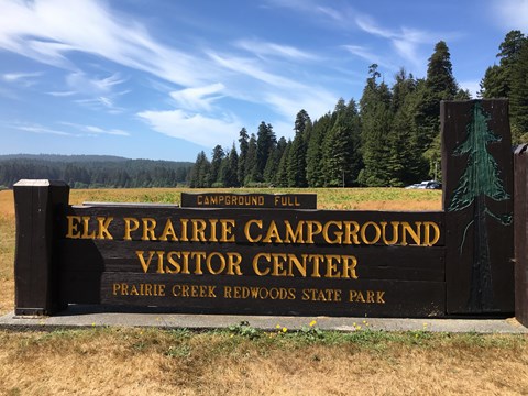 Brown and yellow park sign at the campground edge of a large meadow.