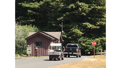 Two vehicles next to a brown building. Redwood trees in the background.