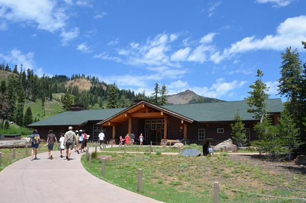 A paved path bends toward a wood building with a green roof backed by mountains