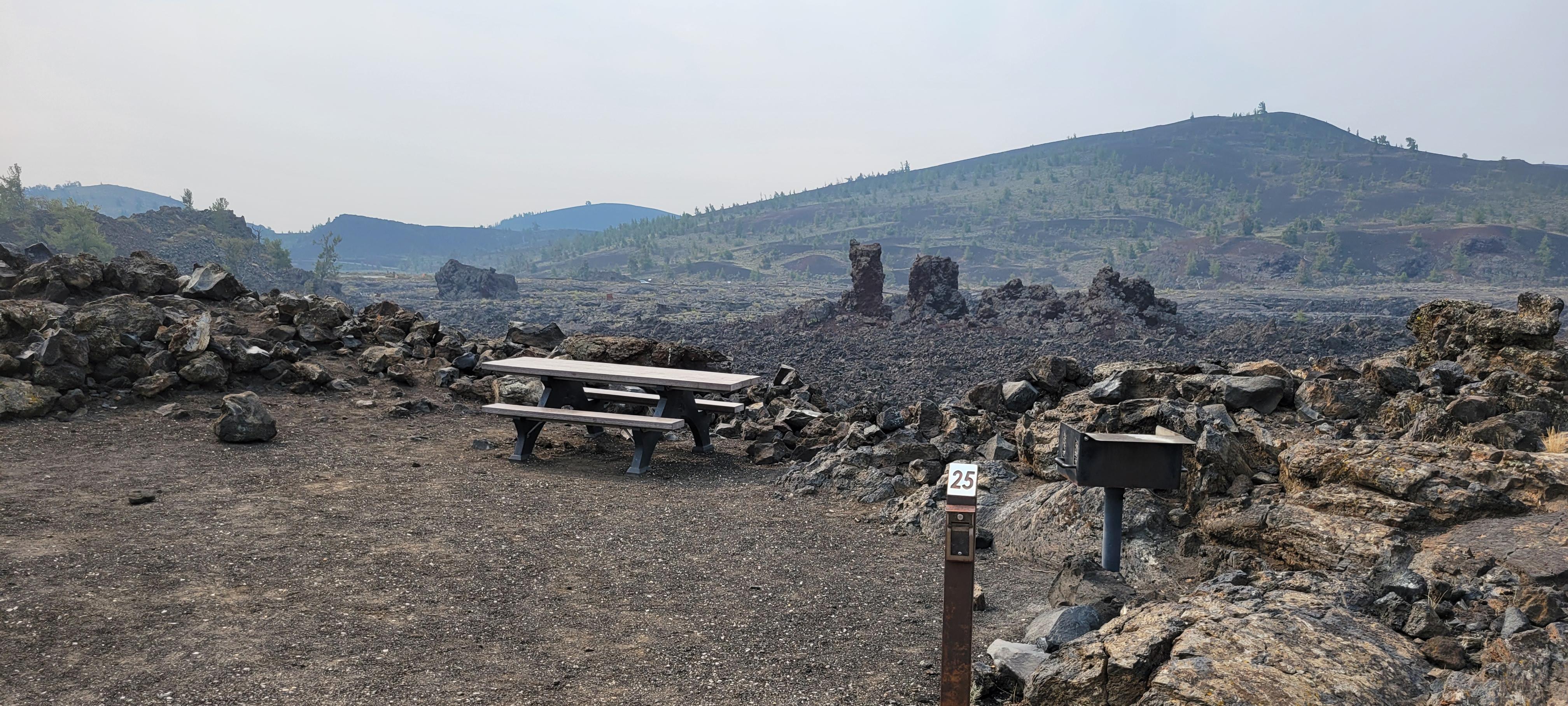 campsite with picnic table and grill against a dark rocky landscape and cinder cones