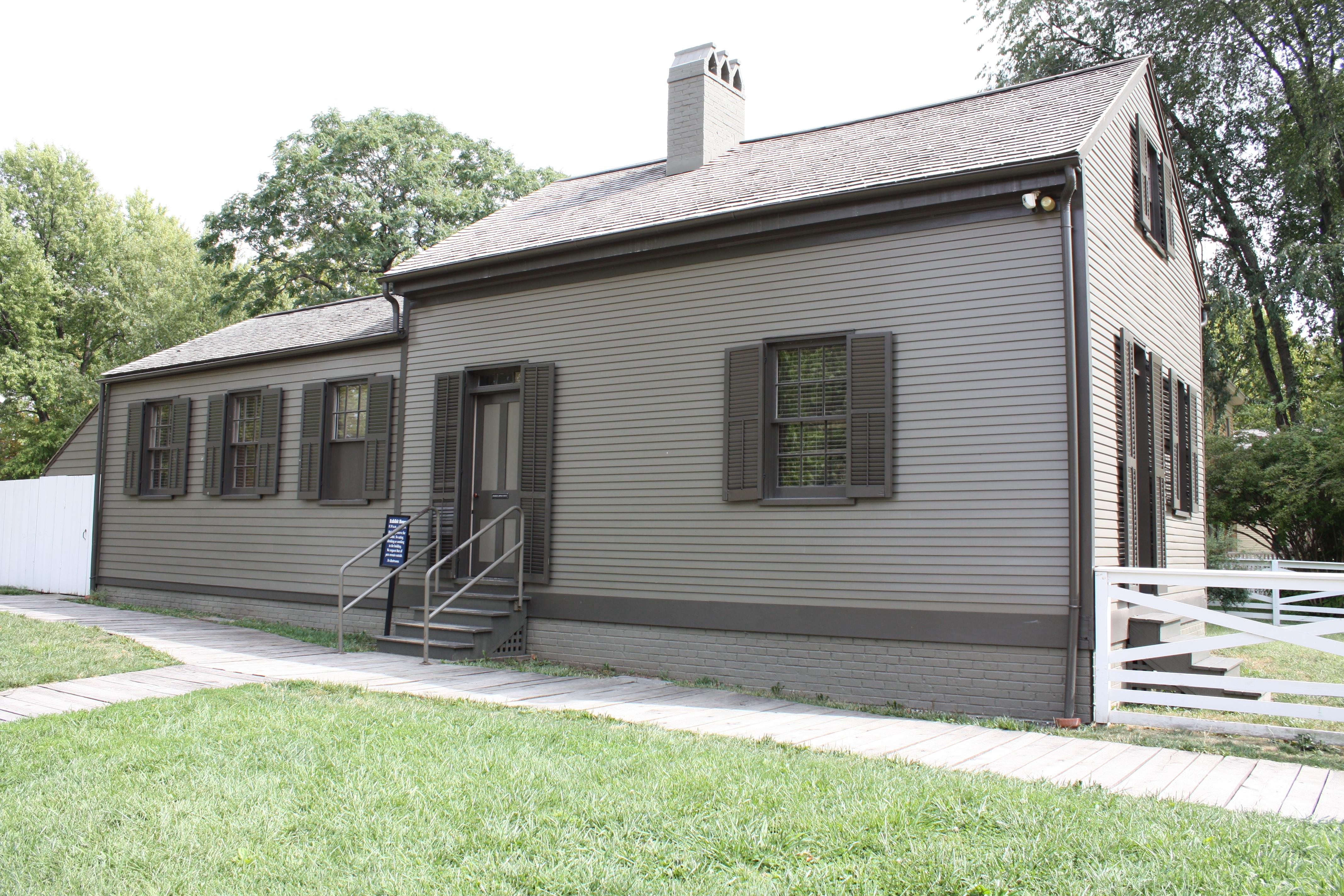 1 story small gray house with stairs leading up to door.