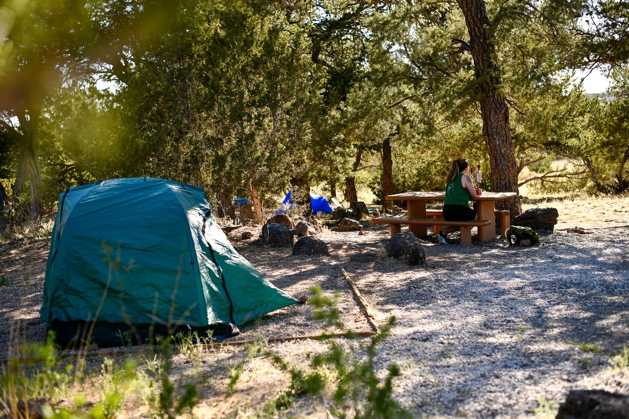A campsite with a tent set up and a person sitting at a picnic table.