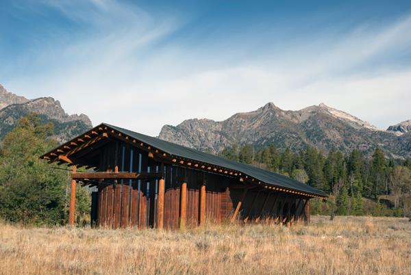 Modern wood clad building with peaked roof in a sagebrush meadow with mountains in the distance