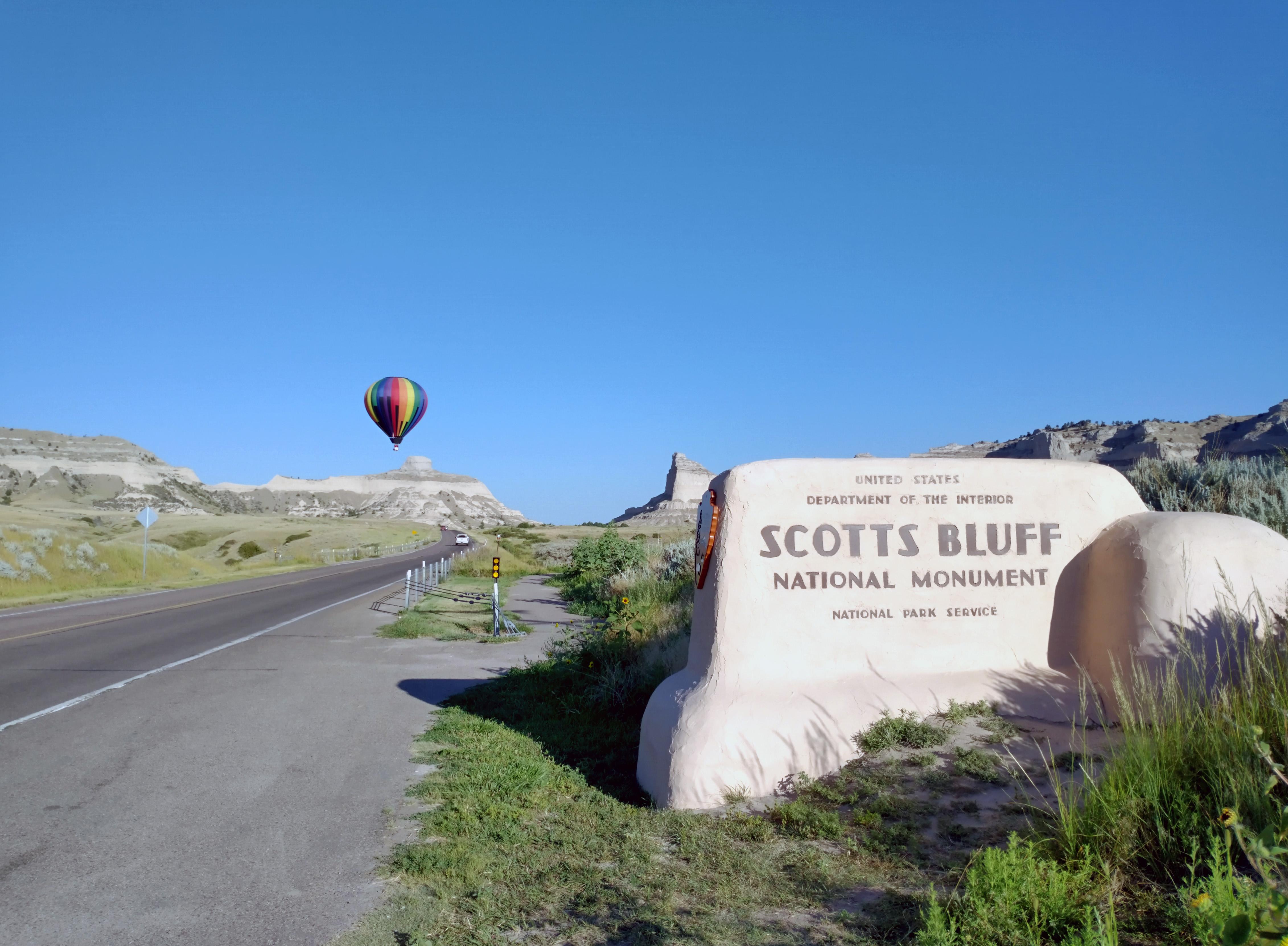 A colorful hot air balloon is seen in the distance with the Scotts Bluff entrance sign.