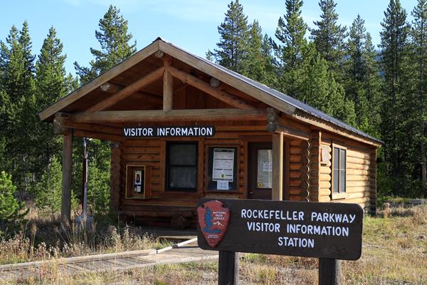 One-room log cabin with wood plank walk and sign out front.