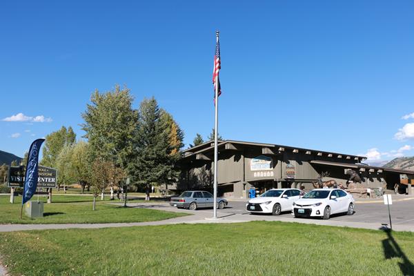 Gray wood shed roof building with parking lot and American flag on pole.